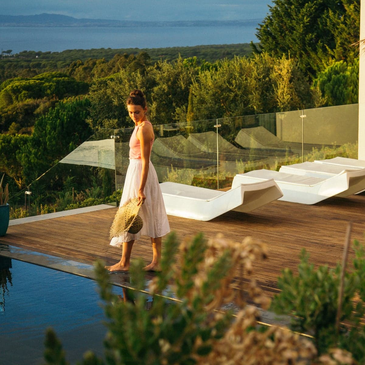 The retreat centre in Portugal: a woman walking along the wooden deck by the pool, with sun loungers beside her and the forest and the sea beyond