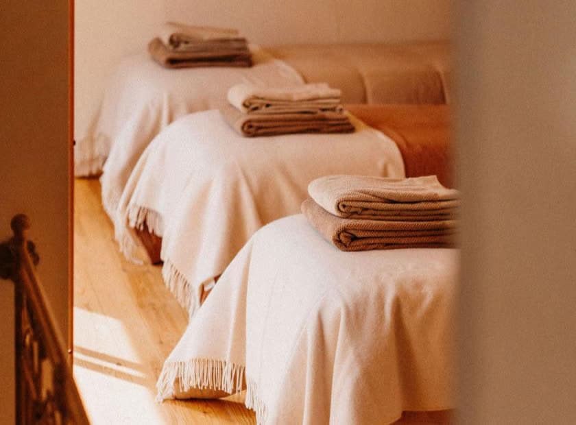 Three beds with folded towels in a warm, sunlit room
