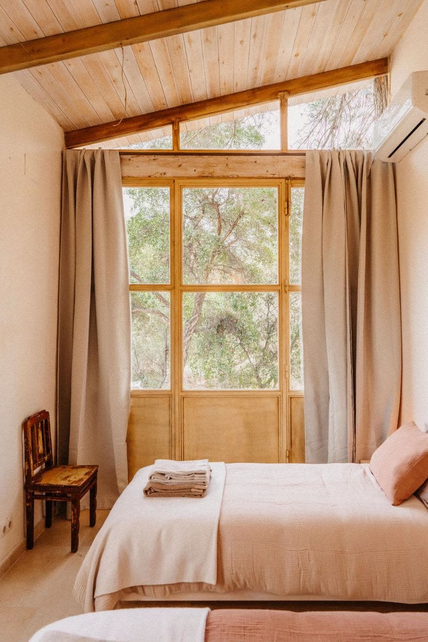 A bedroom with a tall wooden window and linen curtains