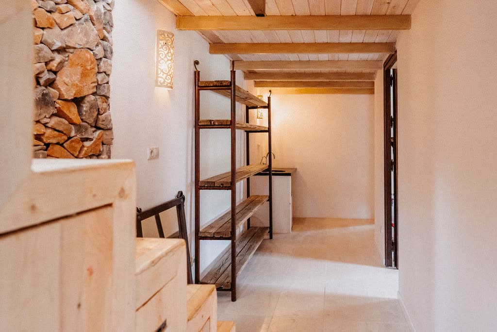 A bright corridor with wooden shelves and a stone wall