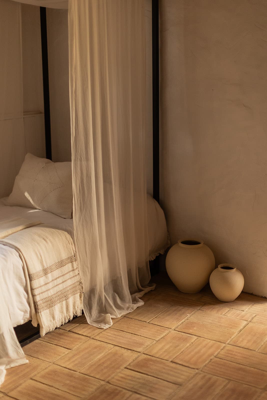 A bed with sheer drapes and clay vases