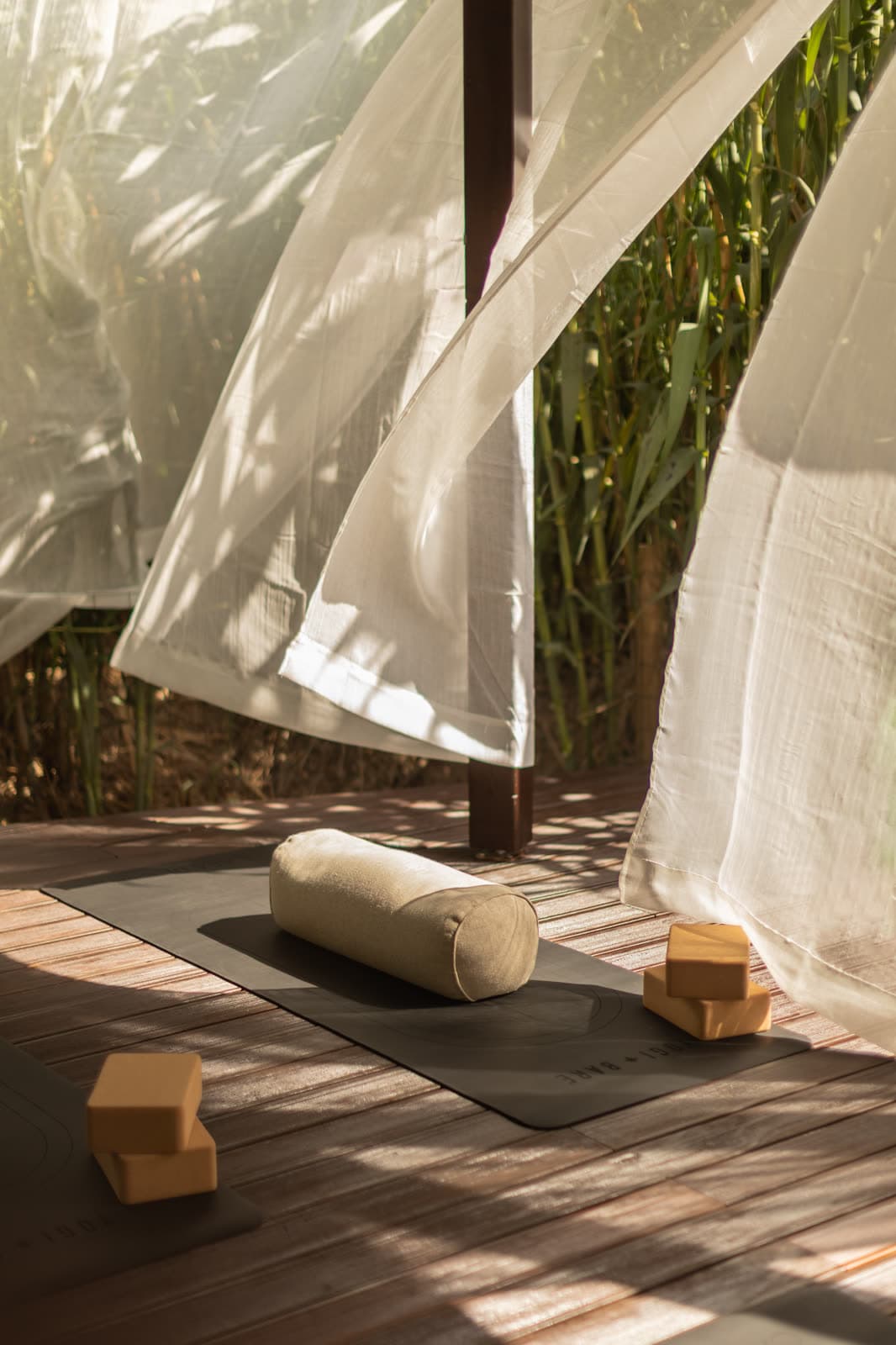 Curtains blowing around a yoga mat and bolster on a deck