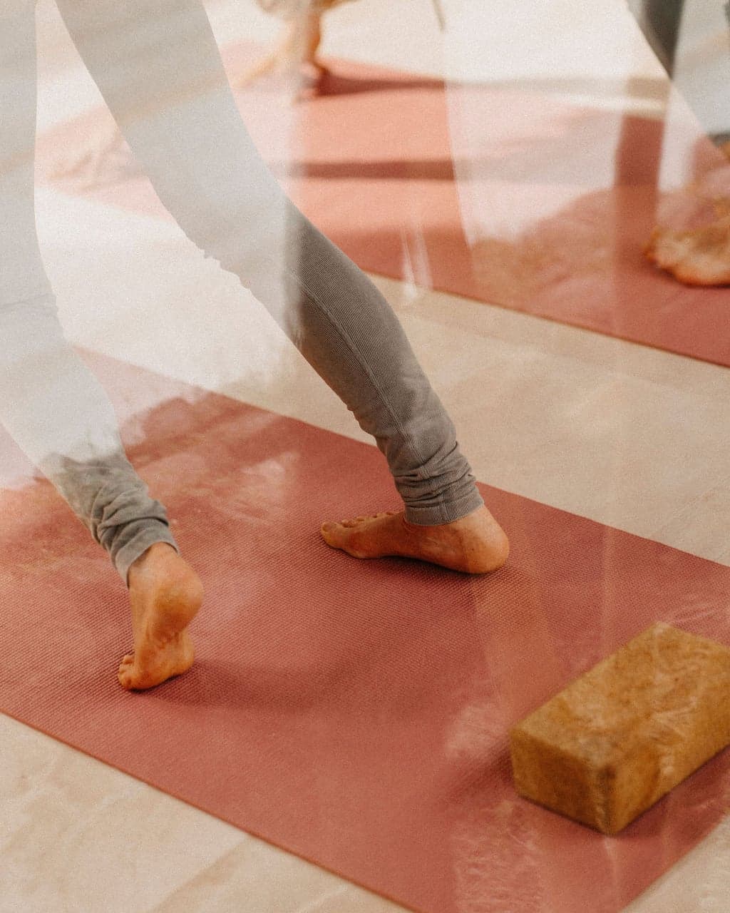 Bare feet stepping across a yoga mat beside a cork block