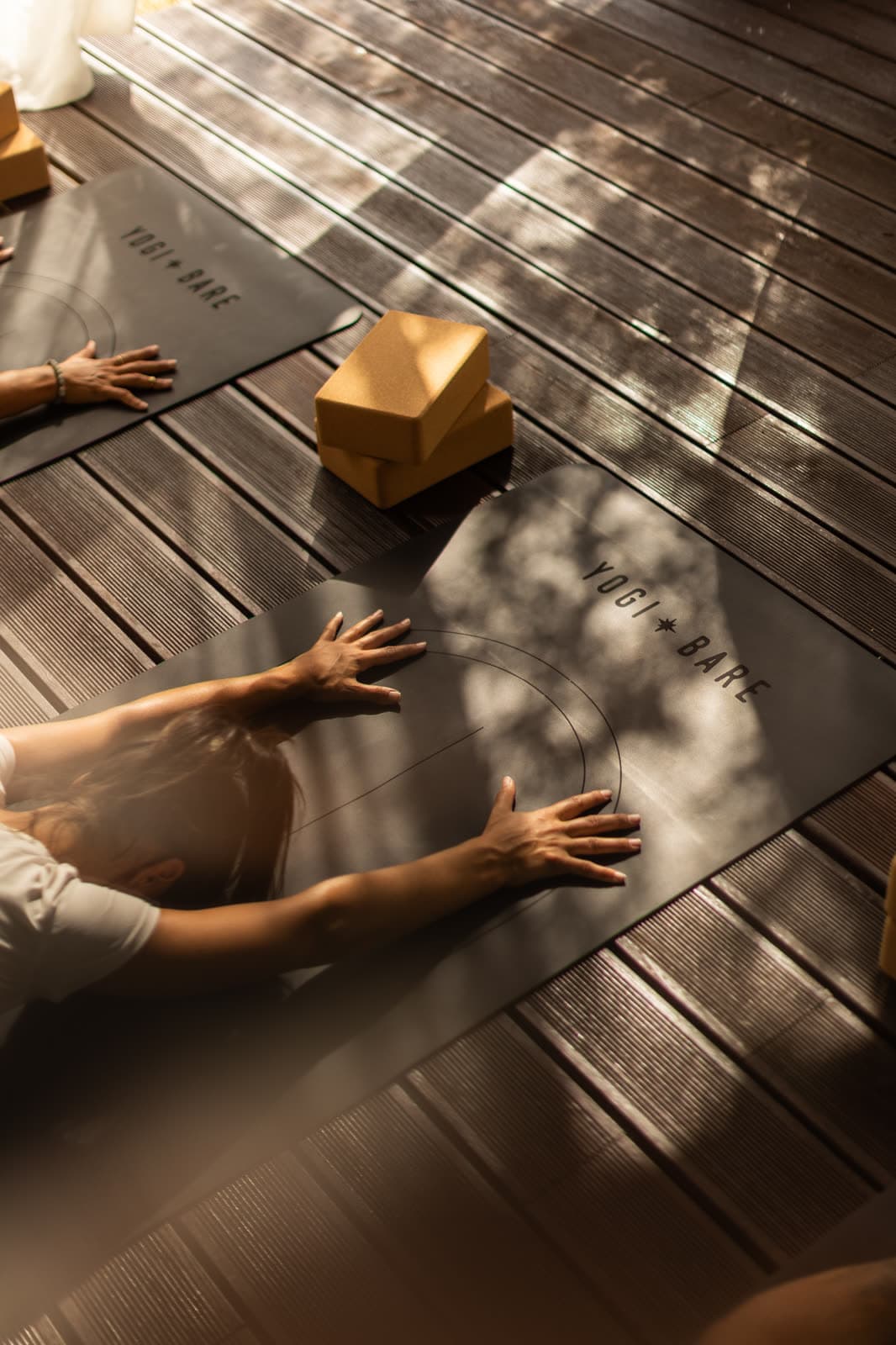 Hands resting on a yoga mat on a sunlit wooden deck