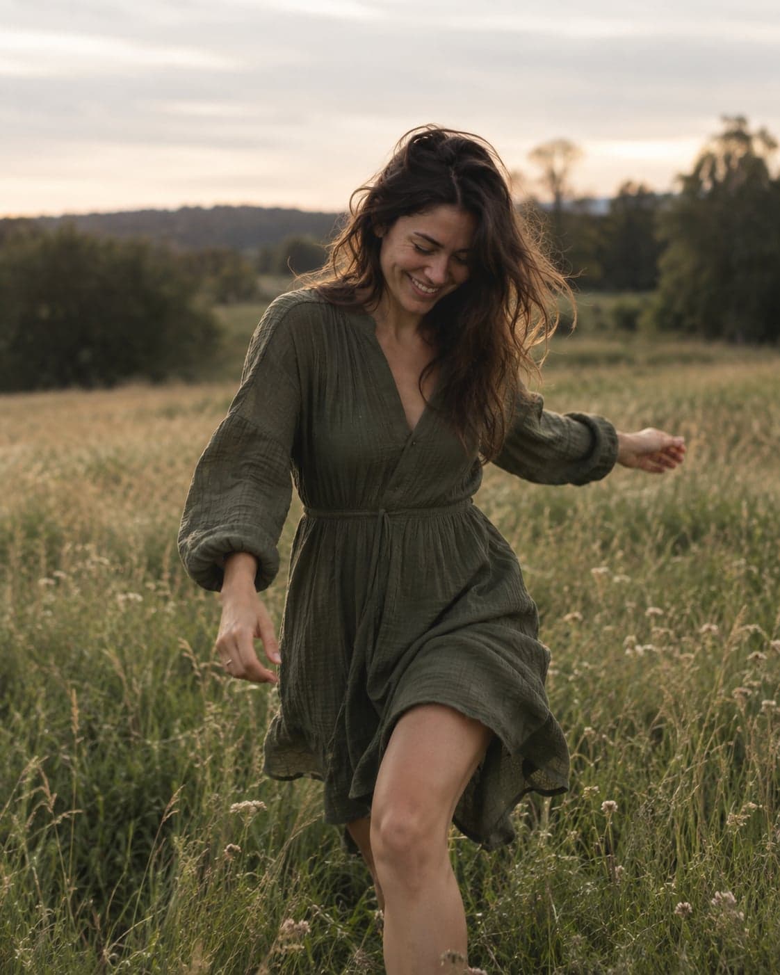 A woman walking through a meadow at dusk, smiling